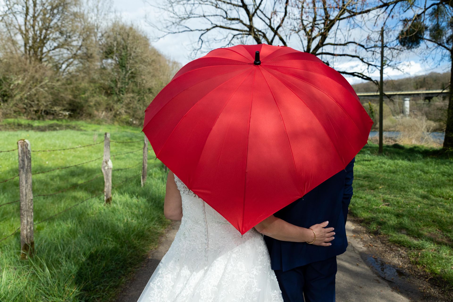 Mariés vu de dos sous un parapluie rouge en forme de coeur. Esther Raguenet Photographie Mariage